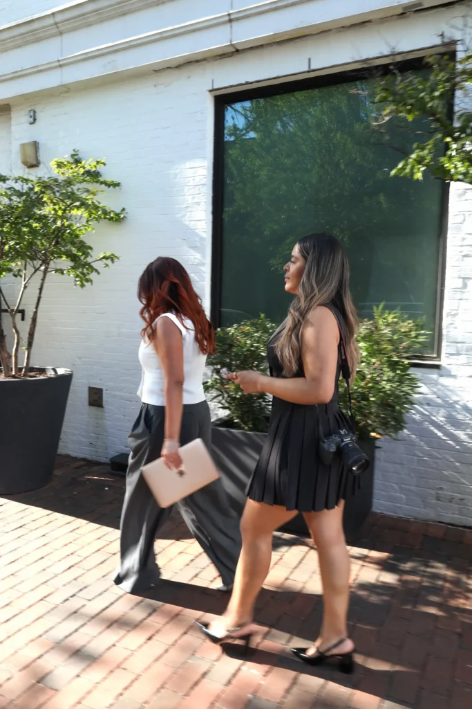 Two women walking on brick sidewalk outside building.