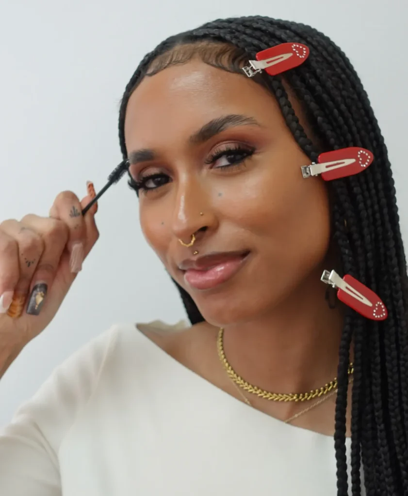 Smiling person applying mascara with braided hair.