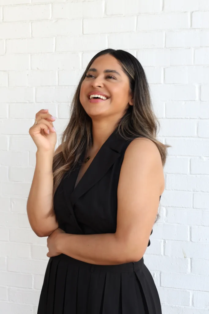 Smiling woman in black outfit against white brick wall.