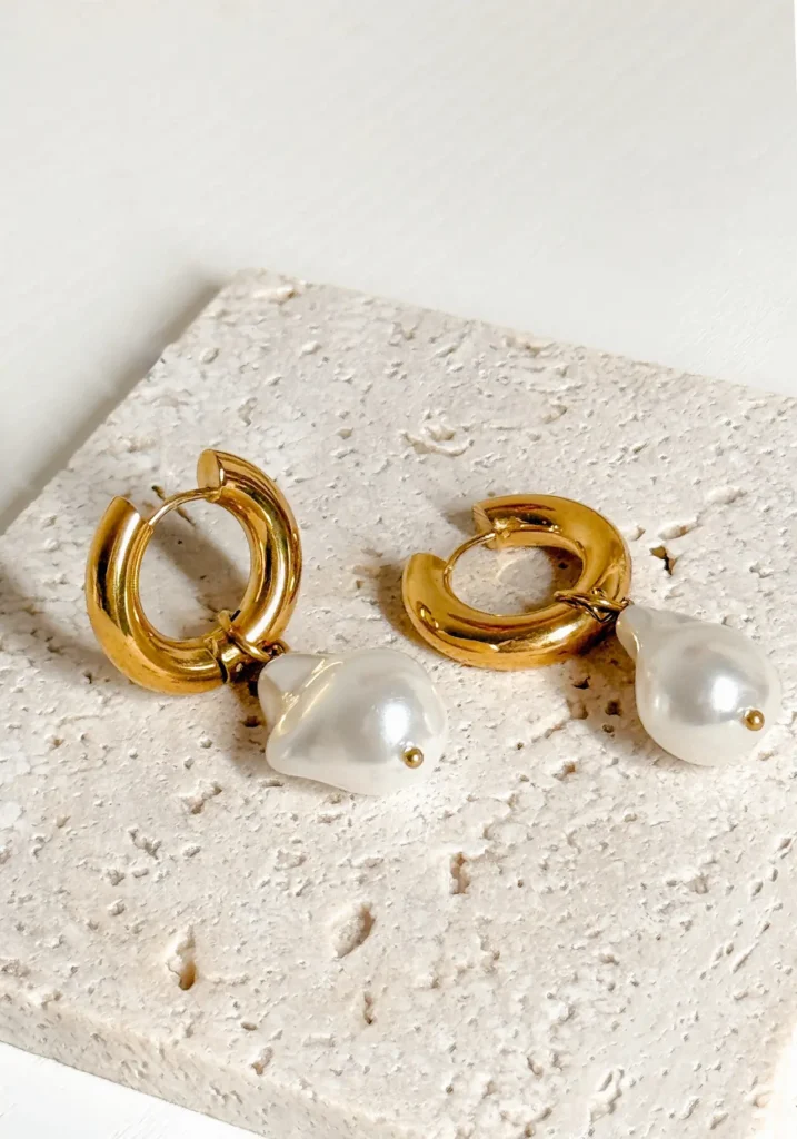 Gold hoops with pearl drops on stone surface.