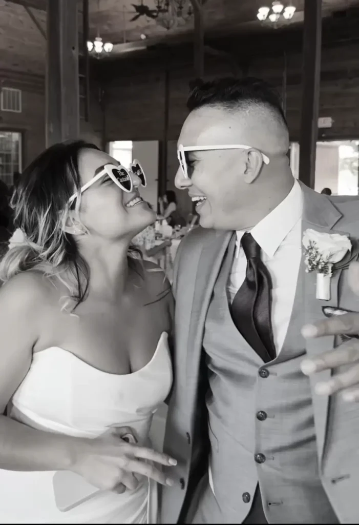 Smiling couple in heart-shaped sunglasses at wedding.
